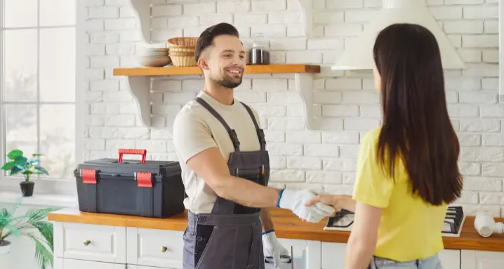 plumber dressed in overalls shakes hands with female client